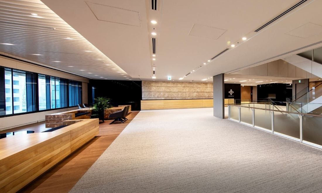 Mitsui & Co.: Carpeted lobby with wooden benches, a stone wall and a glass balustrade