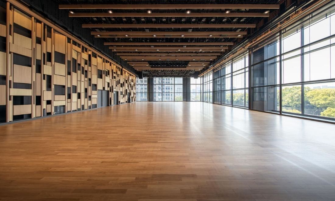 Mitsui & Co.: Empty hall with wooden floor and patterned timber wall beside tall windows