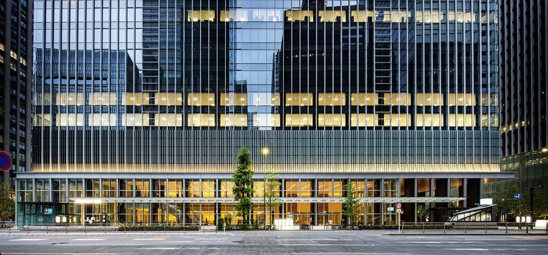Mitsui & Co.: Glazed base of an office tower lit from inside at dusk