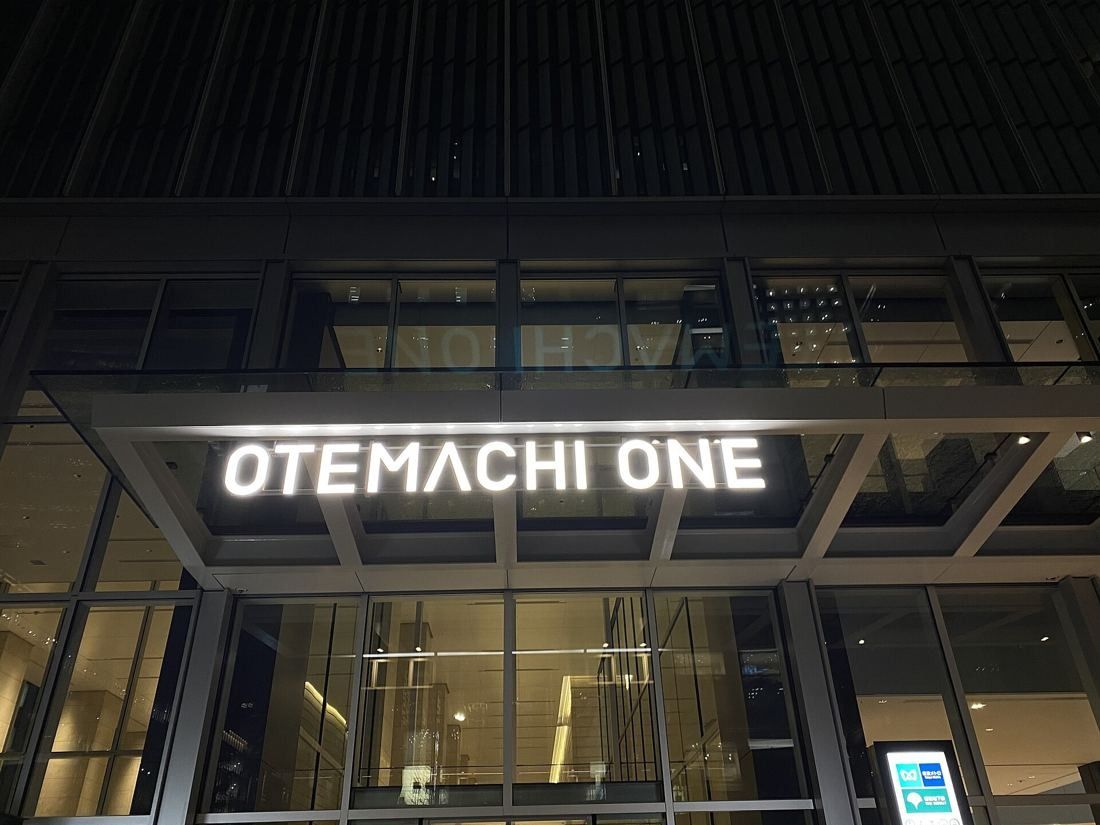 Mitsui & Co.: Illuminated OTEMACHI ONE sign above a glass entrance at night