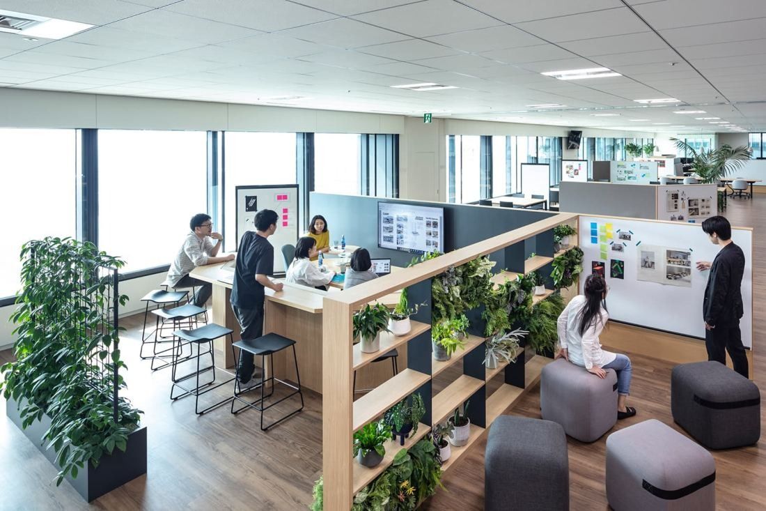 Mitsui & Co.: Standing table and stools behind a shelf of plants, with whiteboards