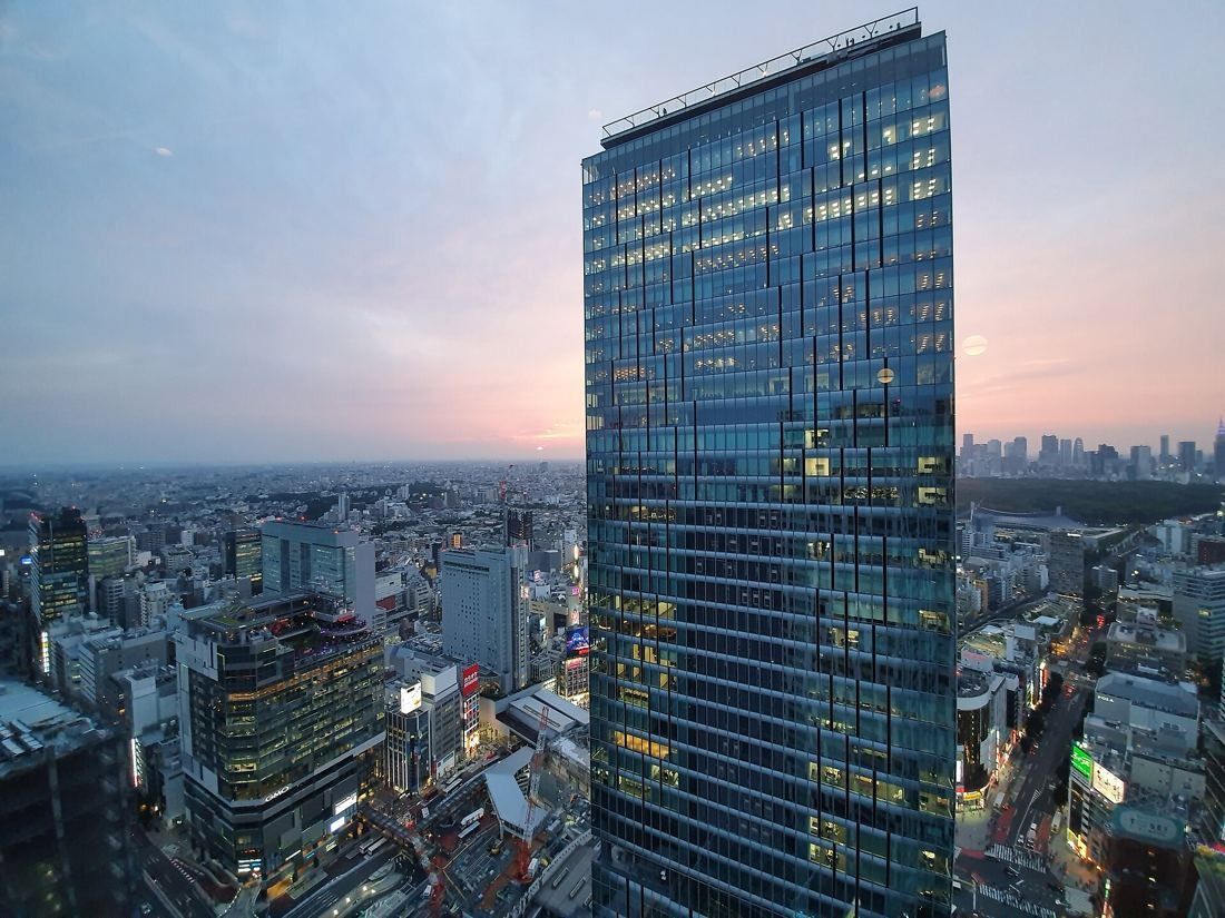 MIXI: Glass tower at dusk with a pink sky over the city