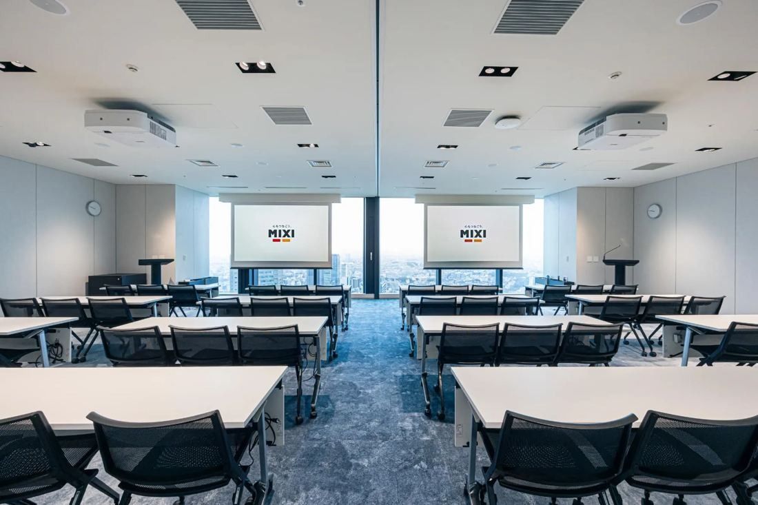 MIXI: Large seminar room with rows of tables and two projection screens
