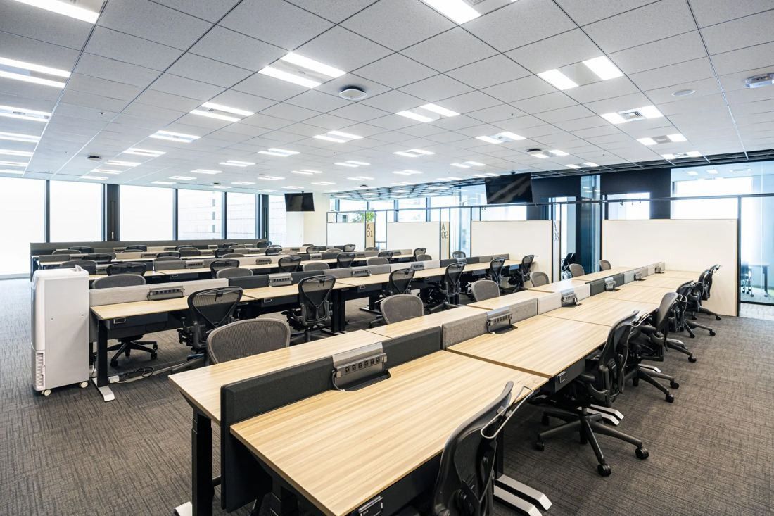 MIXI: Rows of wooden desks with task chairs under bright ceiling lights