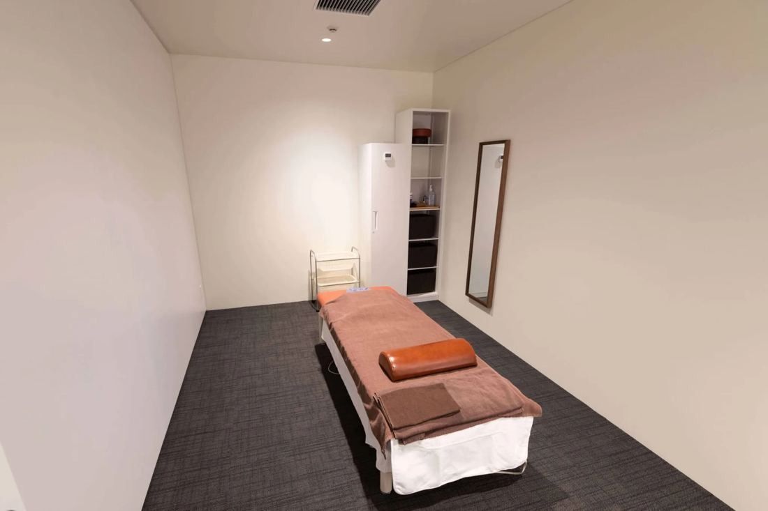 MIXI: Small white room with a massage bed and a mirror
