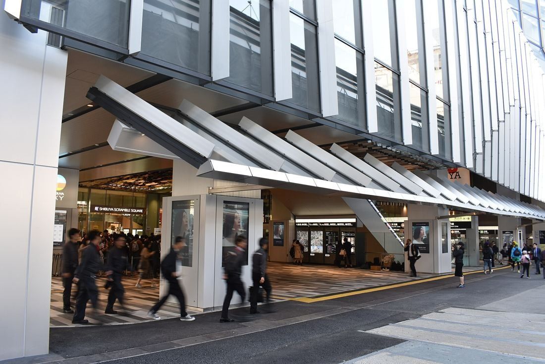MIXI: Street-level entrance with angled canopies and pedestrians walking past