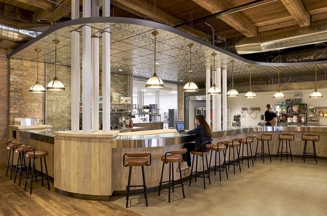 Mondelēz International: Curved wooden counter with bar stools, brass pendant lamps and a pressed-tin ceiling, with a kitchen behind