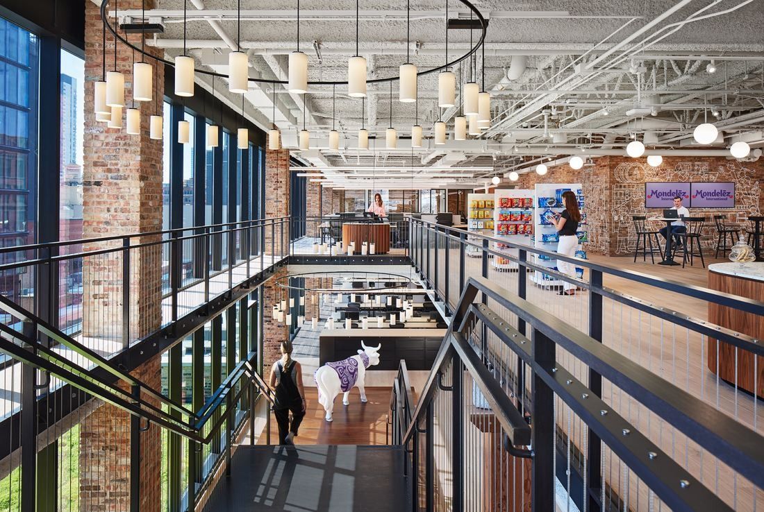 Mondelēz International: Double-height space with a black steel stair, glass walls, brick columns and rows of pendant lights