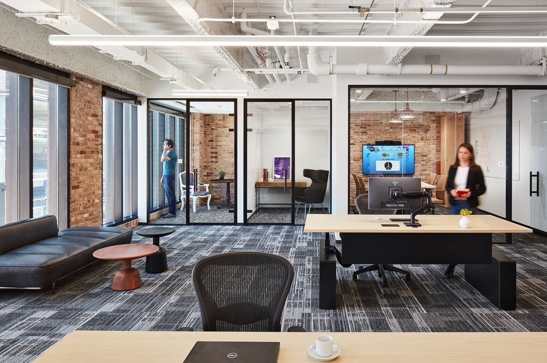 Mondelēz International: Open office with bench desks, a leather sofa and glass-walled small rooms along a brick wall