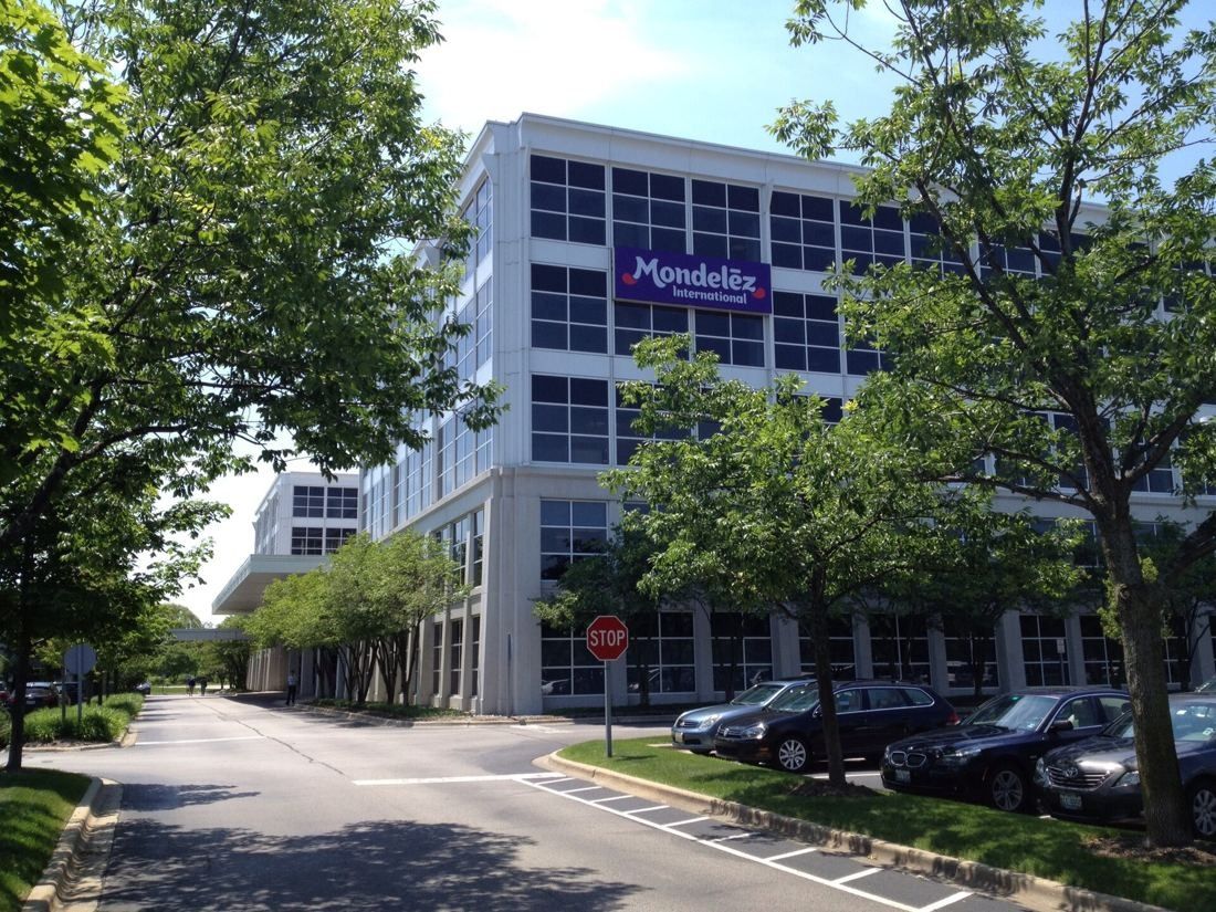 White multi-story office building with a purple sign, seen down a tree-lined driveway