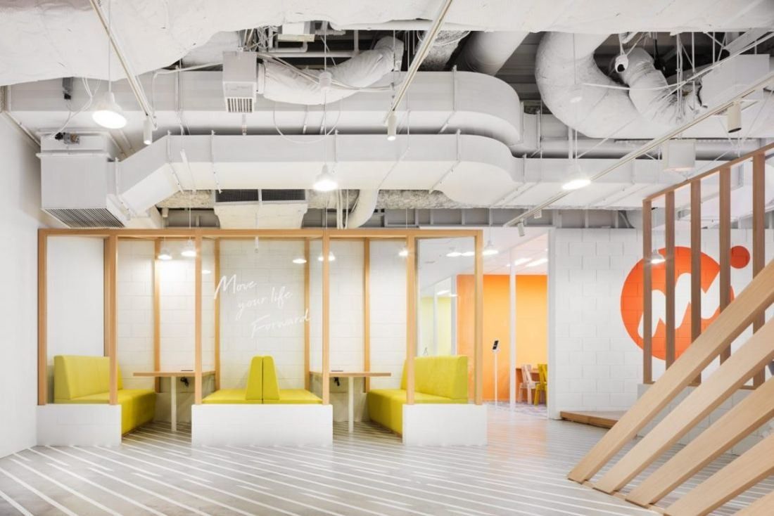 Money Forward: Booth seating in yellow and orange under exposed ceiling ducts, framed by wooden slats
