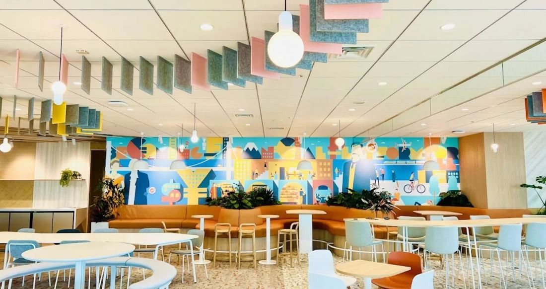 Money Forward: Café-style space with orange benches, white tables, hanging acoustic panels and a colourful illustrated mural