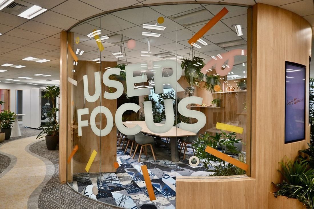 Money Forward: Curved glass wall lettered with large words and confetti graphics, a wooden column and plants