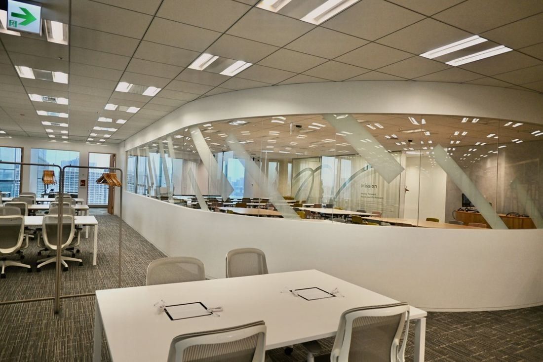 Money Forward: Curved glass-walled room with rows of tables behind a white work table in the foreground