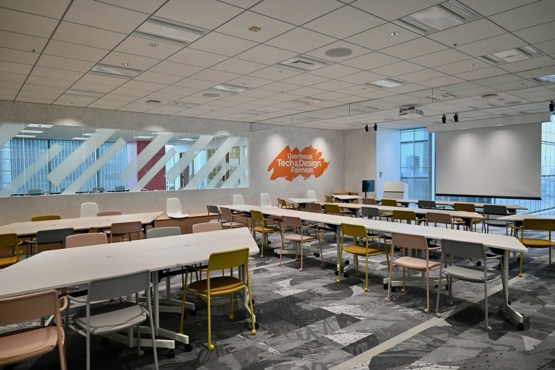 Money Forward: Large room with rows of tables and chairs and a wall graphic at the far end