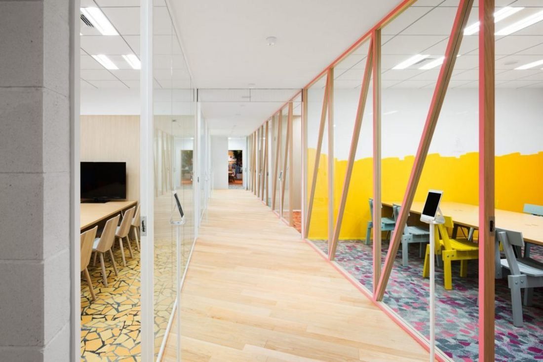 Money Forward: Long corridor with a glass wall and diagonal coral-coloured frames beside a desk area with yellow walls