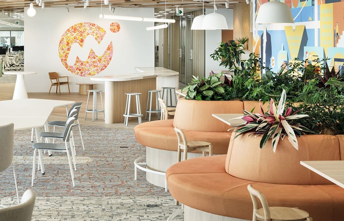 Money Forward: Lounge with round orange banquettes around planters, white stools and a large wall logo made of flowers