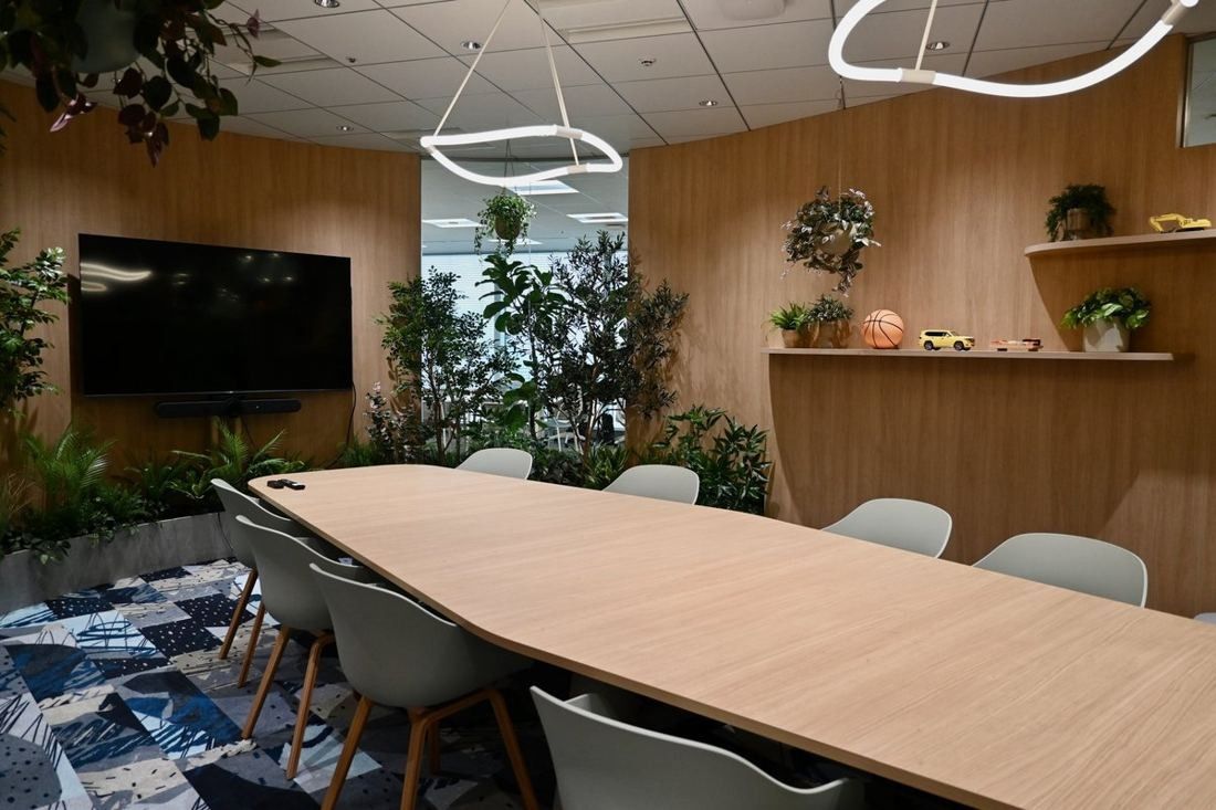 Money Forward: Meeting table with grey chairs, a ring pendant light, wooden walls with shelves and plants