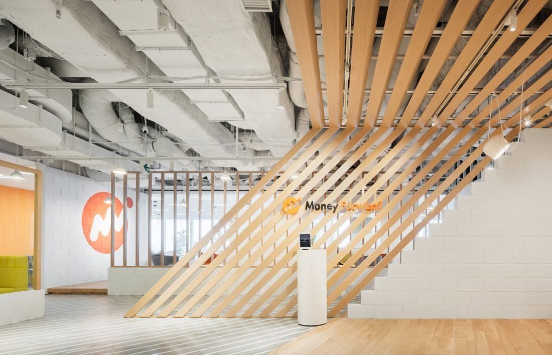 Office entrance with diagonal wooden slats rising from the floor, a white wall with an orange logo and pale wood flooring