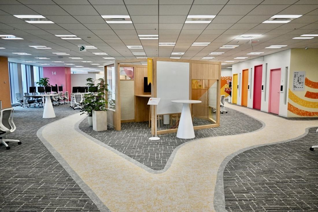 Money Forward: Open office with a winding pale path across grey carpet, wooden booths and colourful meeting-room doors