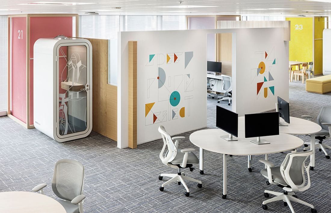 Money Forward: Round desks with monitors separated by white panels printed with colourful shapes, a phone booth behind