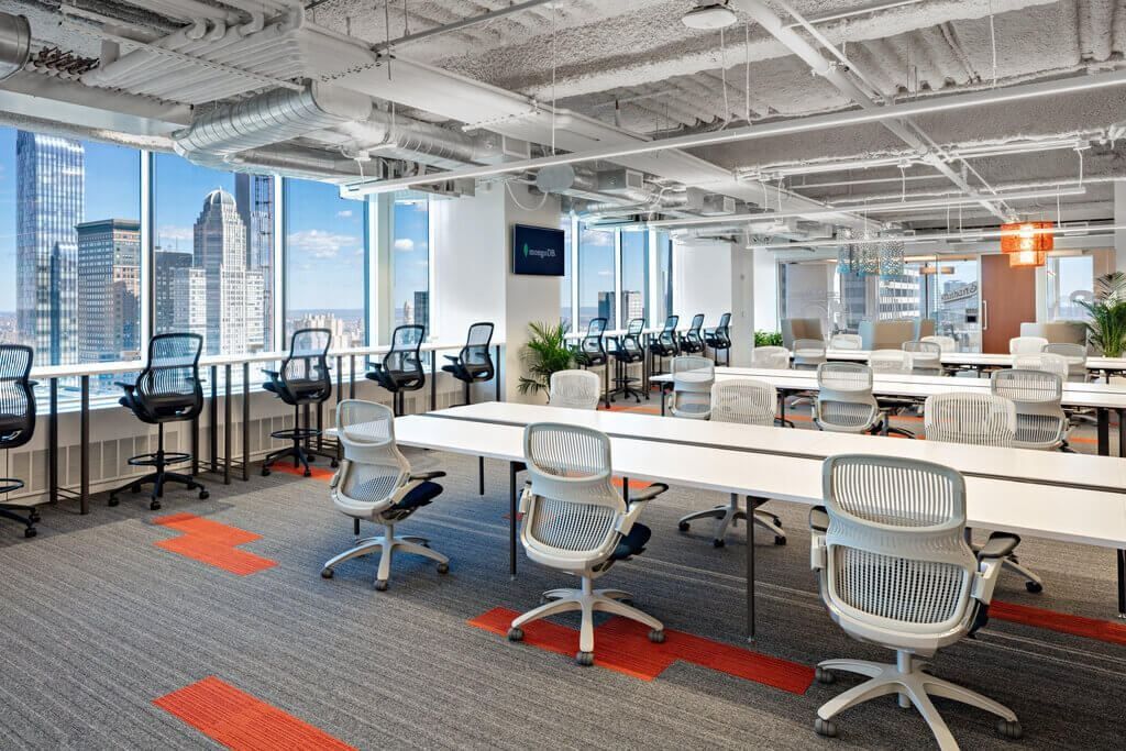 MongoDB: Long white desks with mesh office chairs in an open floor beside tall windows