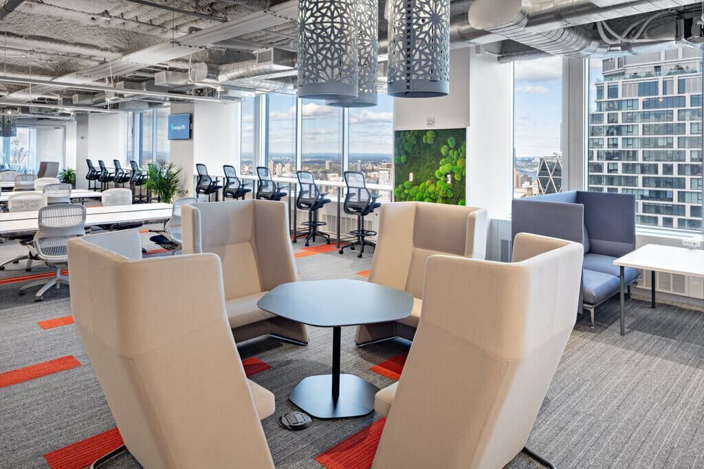 MongoDB: Lounge seating with cream armchairs and a round table near rows of desks and a green plant wall