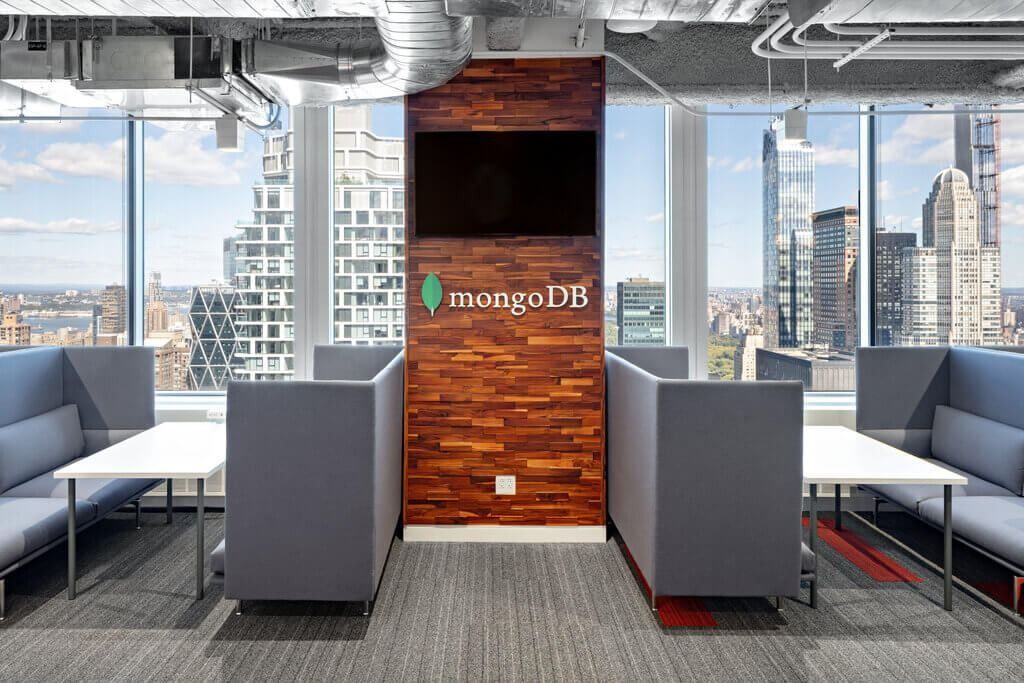 Open office area with grey high-backed booths around a wood-panelled column, floor-to-ceiling windows showing Midtown towers