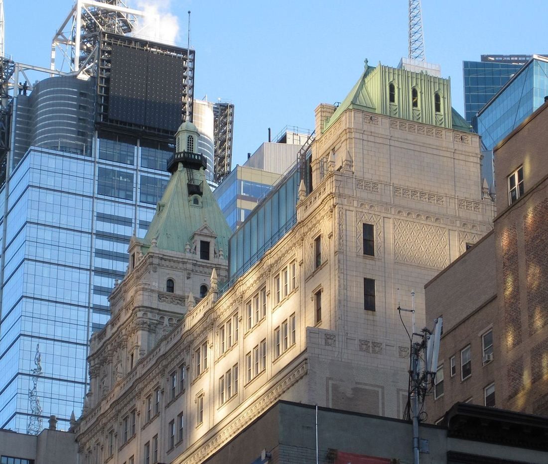 Ornate stone building with green copper roofs between glass towers