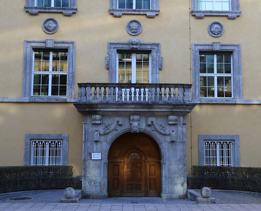 Munich Re: Arched wooden door framed by carved stone and a balcony on a yellow façade