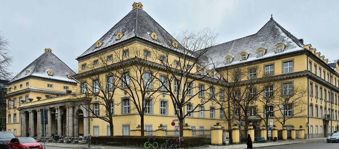 Munich Re: Corner view of a long yellow building with steep slate roofs behind bare trees