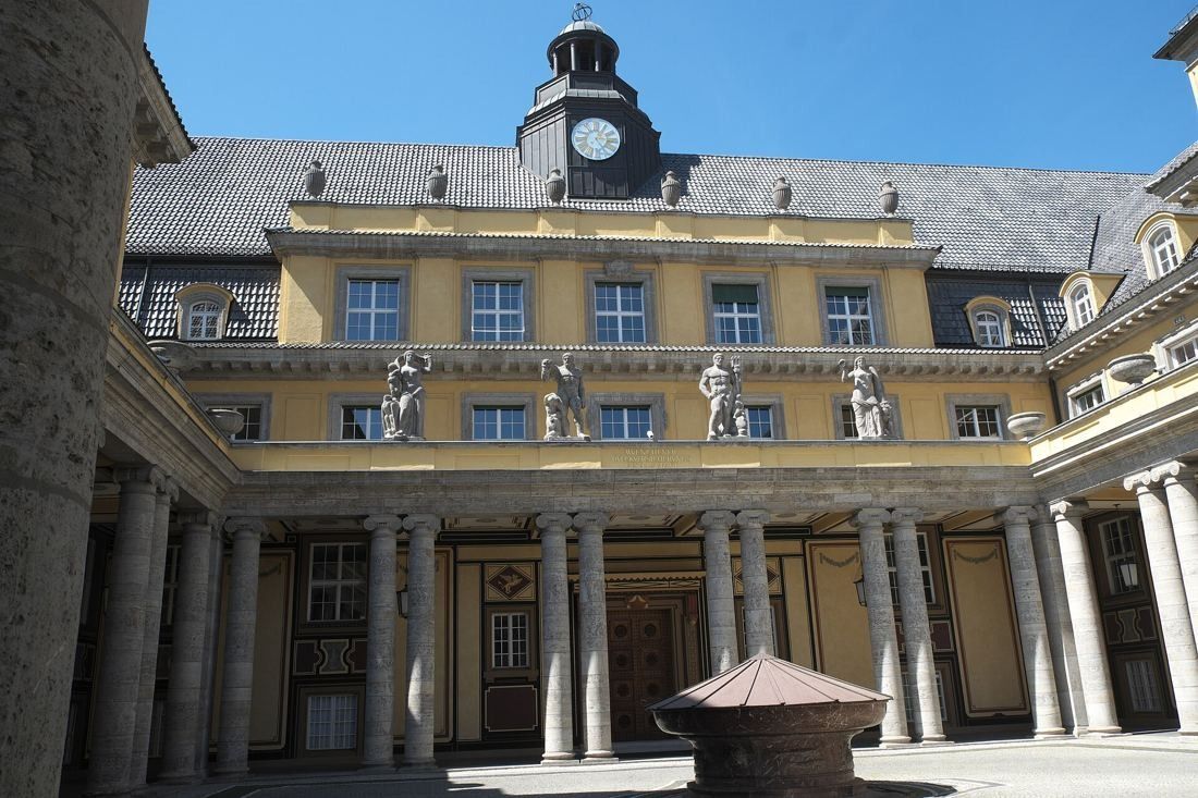 Munich Re: Courtyard ringed by stone colonnades with statues on the balustrade and a clock turret above