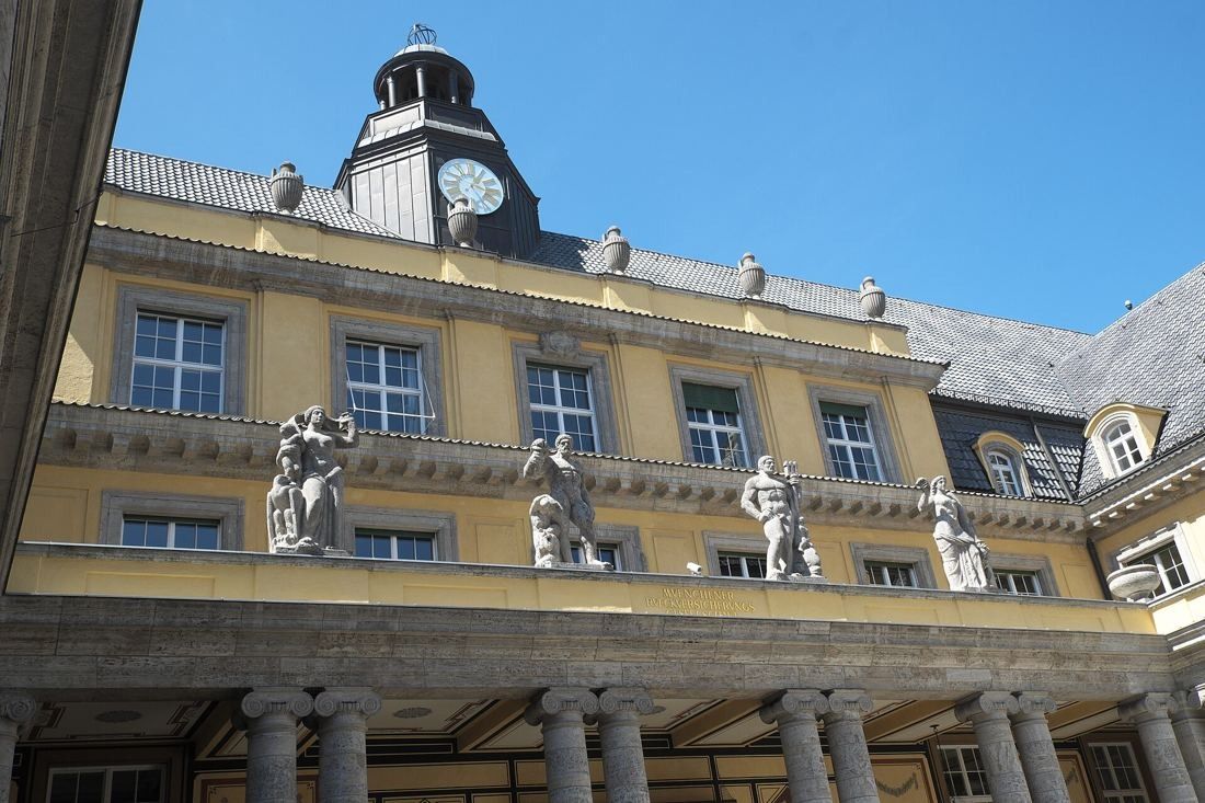 Munich Re: Four stone statues standing on a balustrade above a colonnade, clock turret above