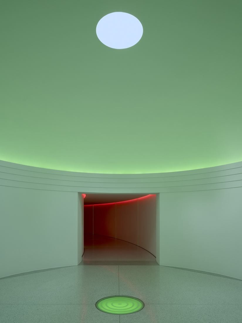 Munich Re: Round pale green room with a circular opening in the ceiling and a red-lit passage beyond