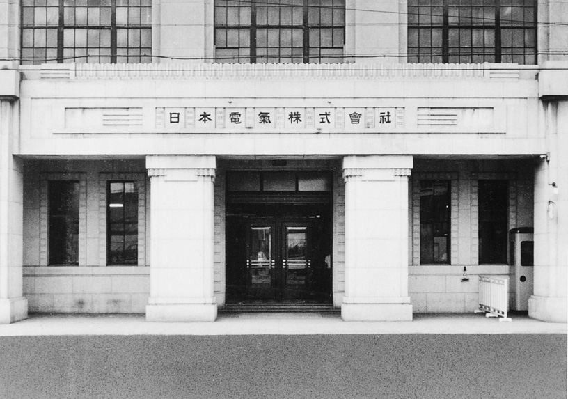 Black-and-white photo of a stone building entrance with columns and a name plate above the door