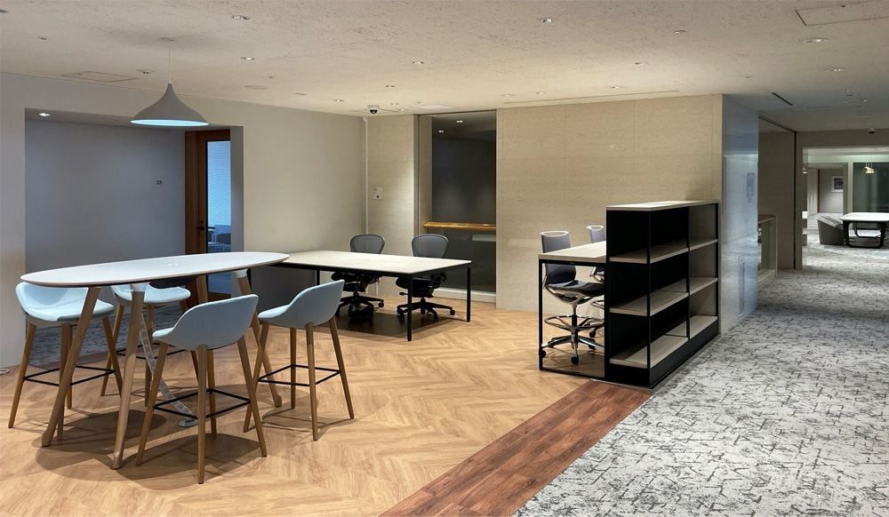 NEC: High table with light-blue stools on a herringbone wood floor, with shelving behind