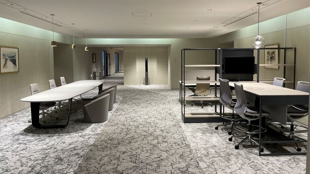 NEC: Long meeting table with tub chairs next to desks and a wall-mounted screen