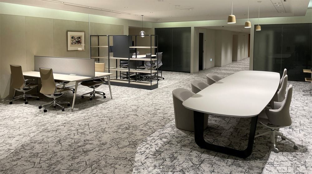 NEC: Lounge with a long curved table, upholstered chairs, open shelving and desks on a patterned carpet