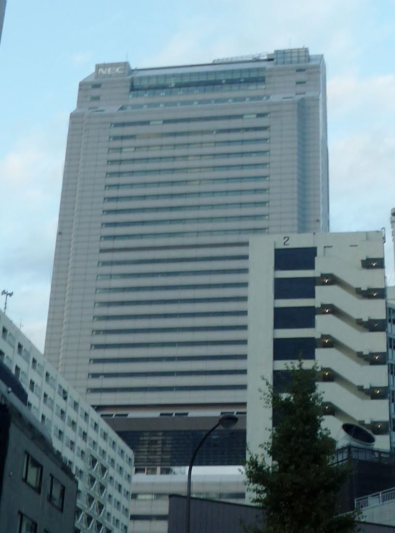 NEC: Pale tower facade rising behind lower buildings