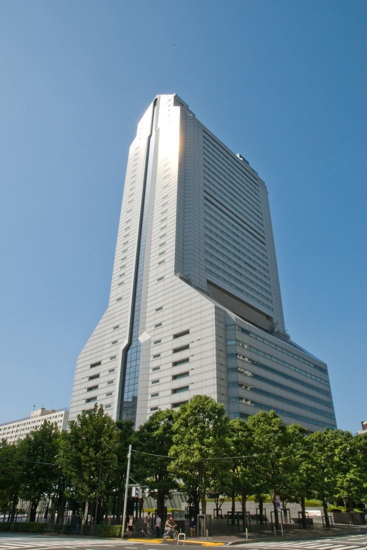 NEC: Tapering tower above a row of green trees under a blue sky