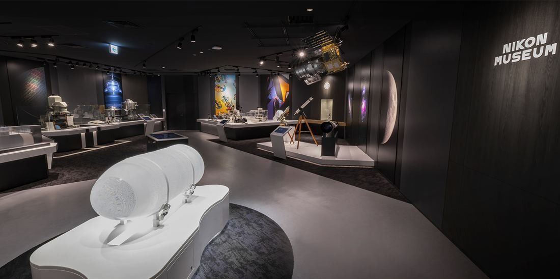 Nikon: Dark exhibition room with a large white lens display on a plinth