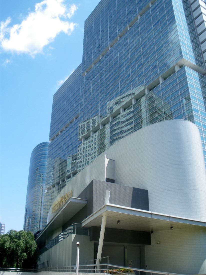Glass office tower with a curved white base next to a second tower