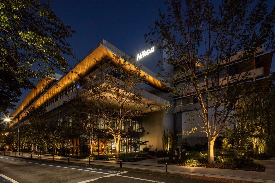 Nikon: The building lit up at dusk, with lit eaves and trees in front