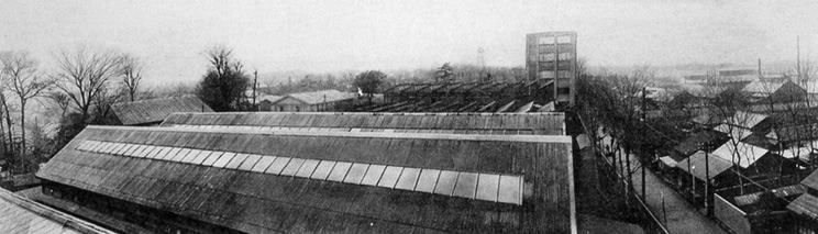 Wide view of long low factory sheds on open land