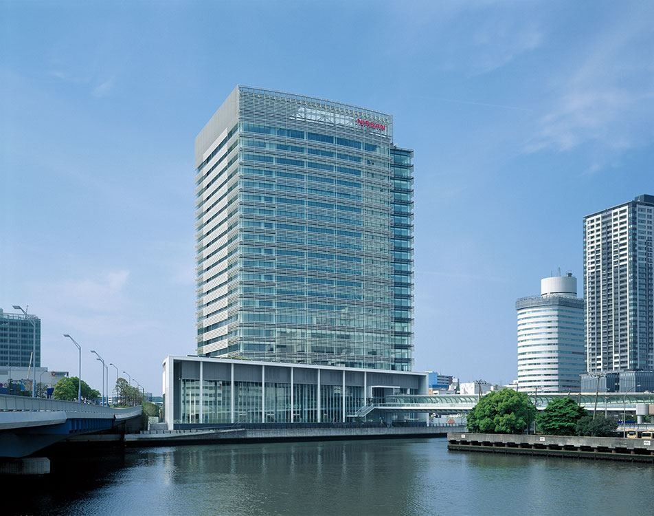 A 22-storey glass office tower with a low white podium beside a canal, under a blue sky
