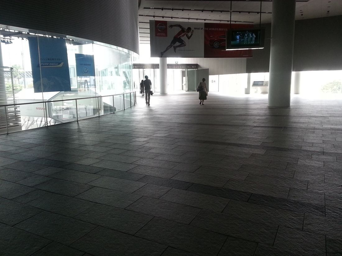Nissan: Dim stone-paved hall with a curved glass wall on the left and daylight at the far end