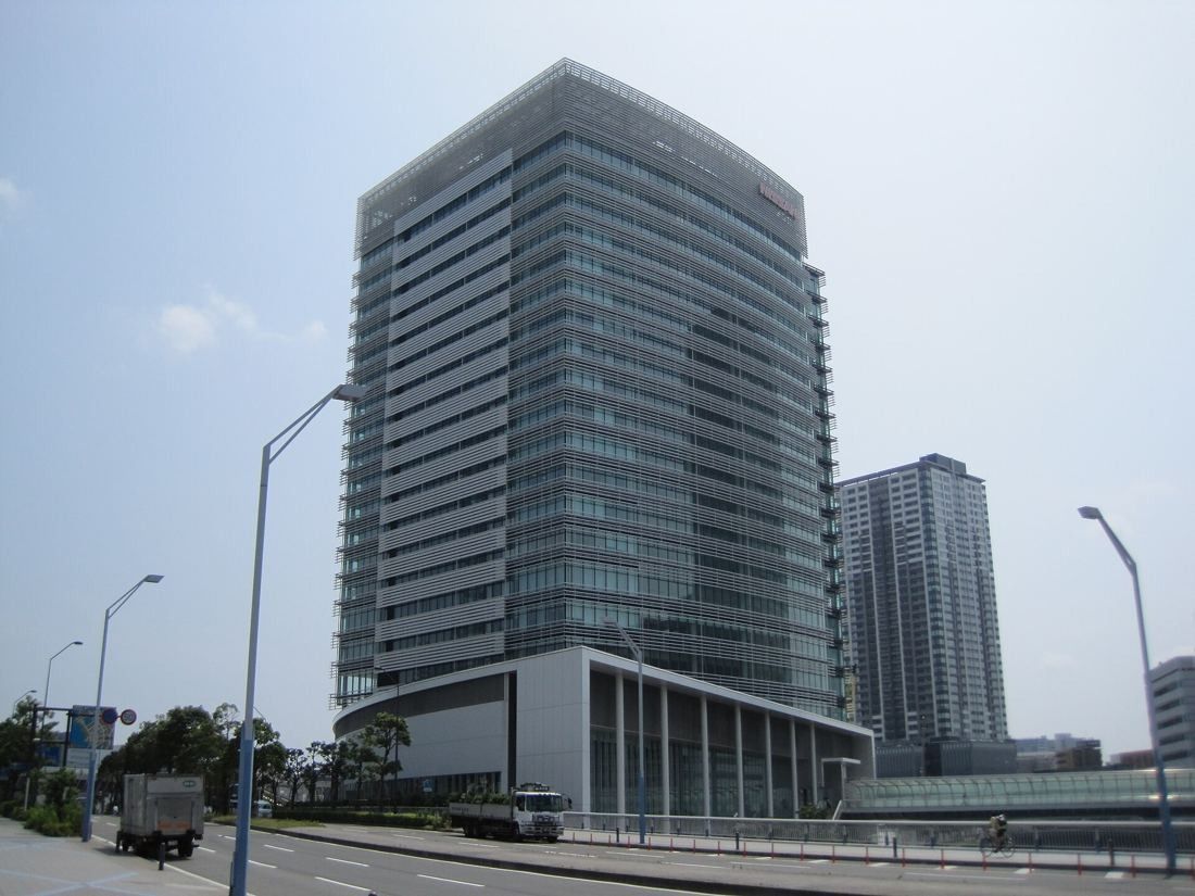 Nissan: Glass office tower seen from a wide road with street lamps