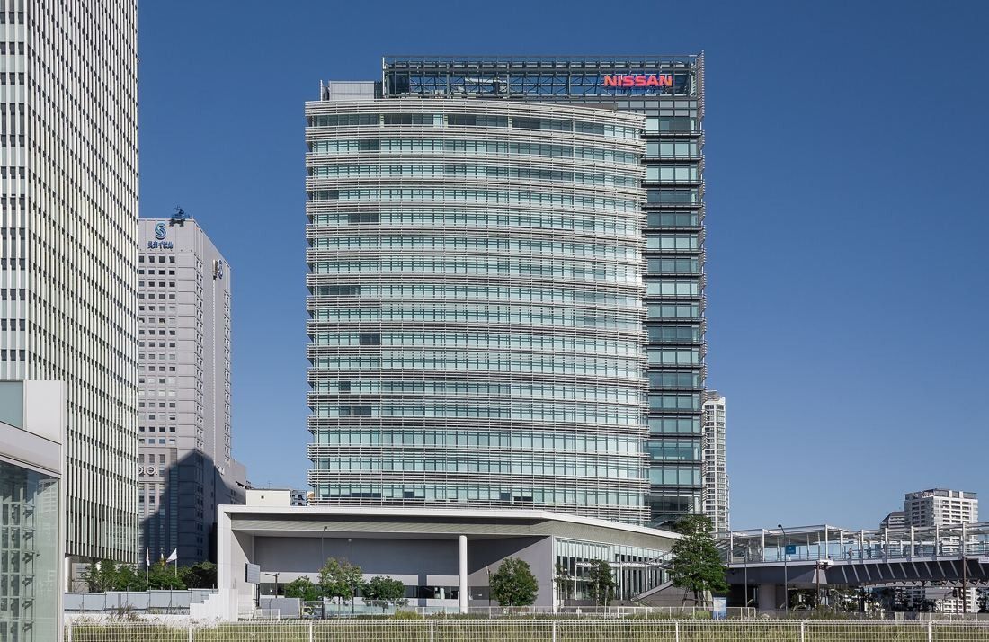 Nissan: Glass office tower with a red logo on top, seen across open ground