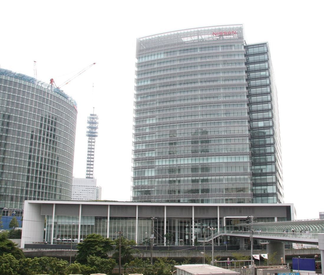 Nissan: Glass tower behind a long low podium and a footbridge, with a crane in the distance