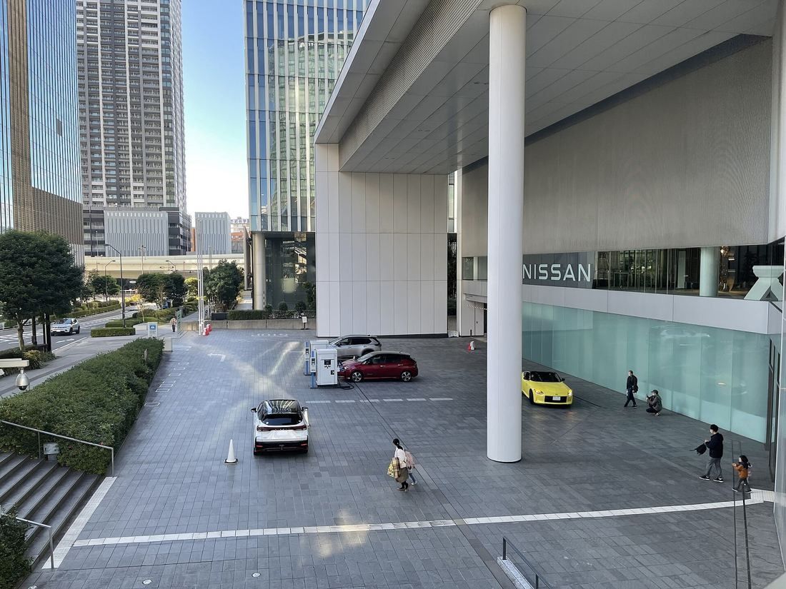 Nissan: Paved forecourt under a tall white column and canopy, with charging stations and parked cars